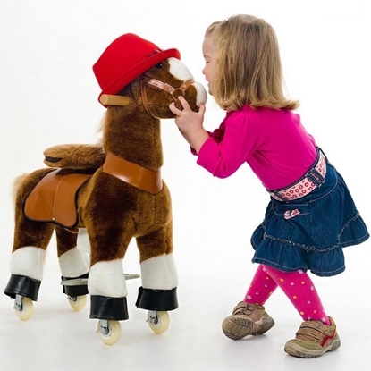 Petit cheval en pluche brun sur roulettes que l'on peut monter.  Il porte un chapeau rouge. Une petite fille lui tient la tête et lui sourit.