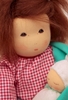 Close up du visage d'une poupée de chiffon aux cheveux de mohair brun et aux yeux bruns, portant son bébé dans las bras. Elle porte une blouse à carreaux rouge et blanc.