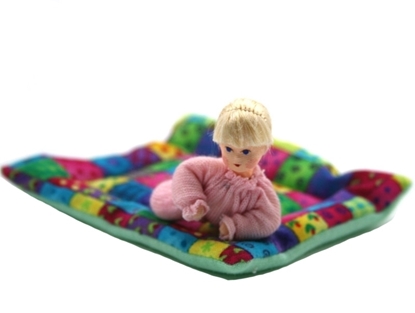 Een blond baby popje met roos kruippakje ligt op een veelkleurig patchwork deken.