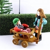Doll for dollhouse, boy with red thick sweater sitting in a wooden cart dragged by his dollhouse sister.