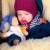Un bambin est en train de dormir en tenant dans ses bras un doudou plat pour dormir Nanchen avec long bonnet bleu.